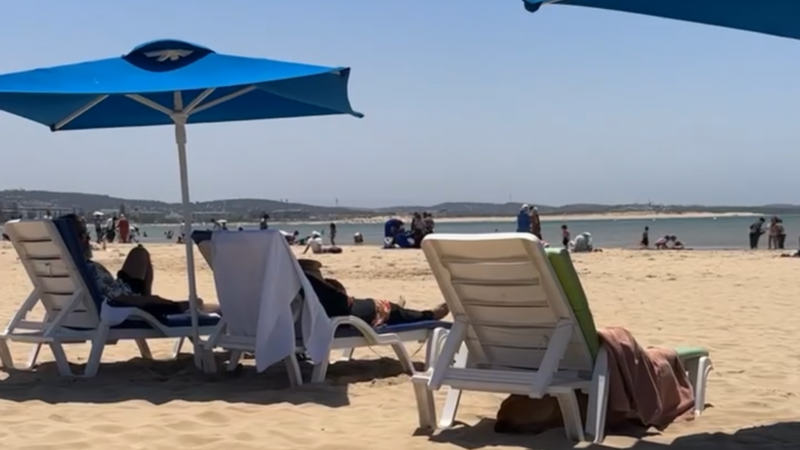 jungen-maedchen-erziehung-strand-essaouira.jpgeinem blauen Sonnenschirm an einem belebten Sandstrand